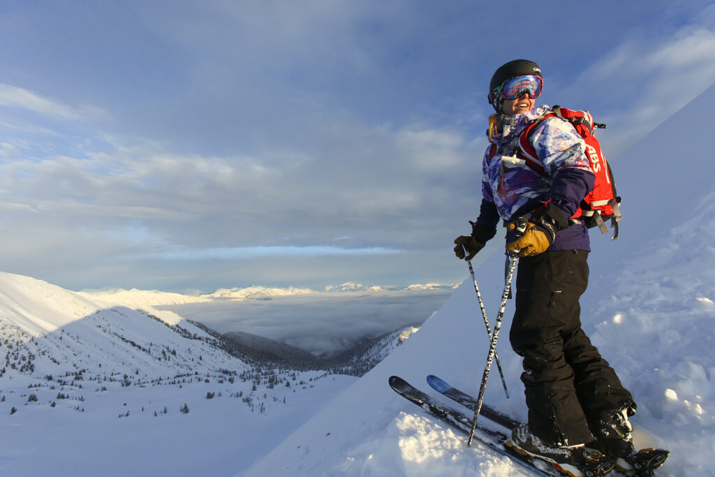 skier ingrid backstrom in the mountains, looks over her shoulder beyond camera, smiling