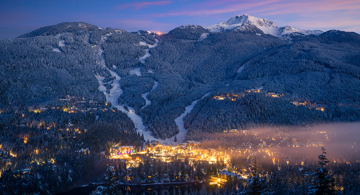 whistler ski resort at dusk covered in snow with lights shining out from the town in the distance