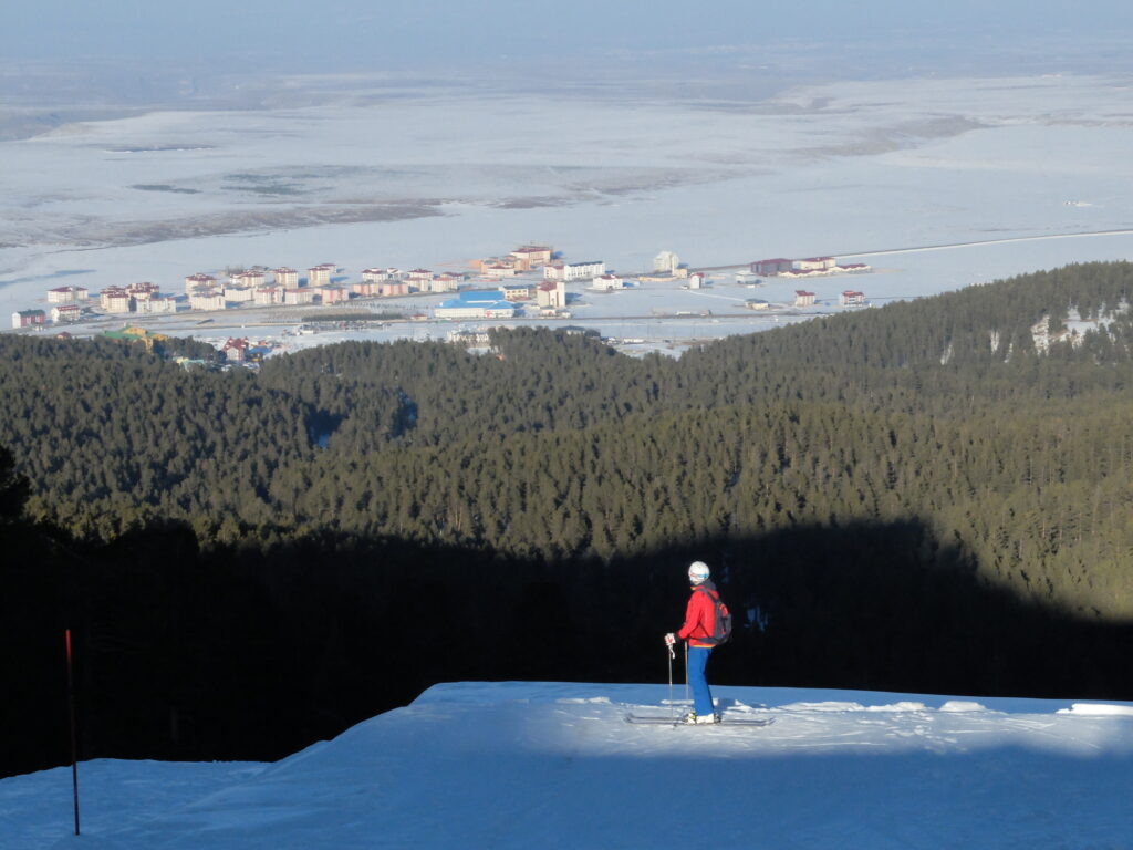 skier looks over Sarikamis ski base far beneath, on the other side of a green huge forest