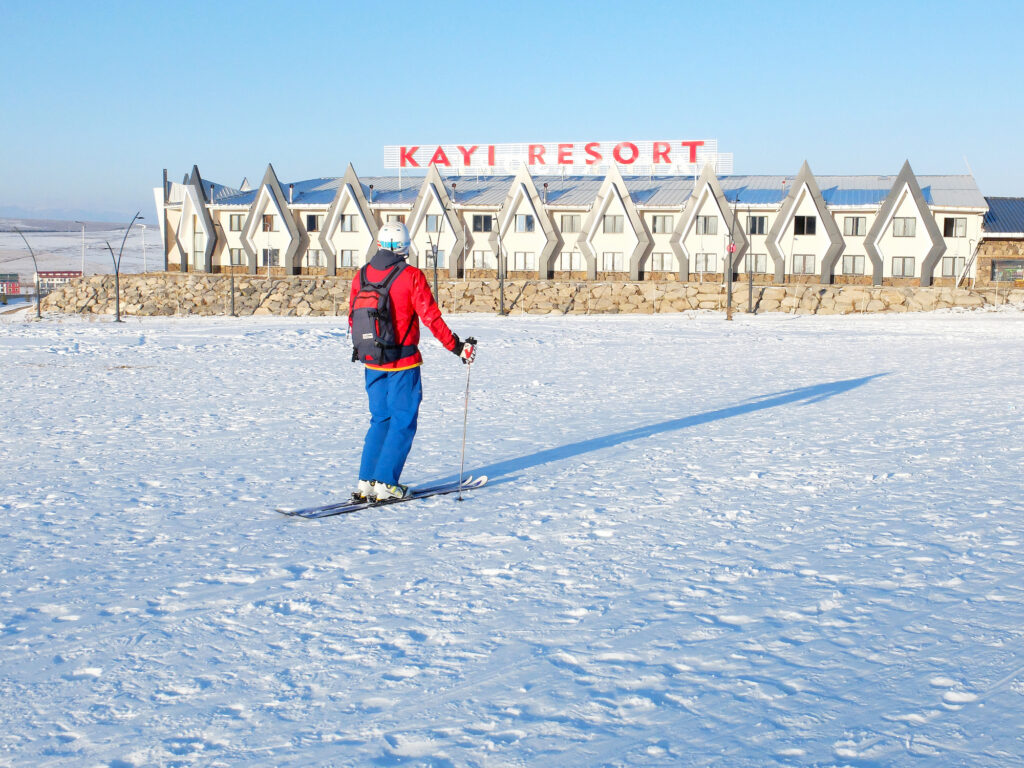 skier stands on flat snow looking at ski resort buildings