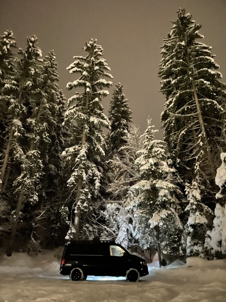 camper van parked in very snowy setting, in front of snow laden trees