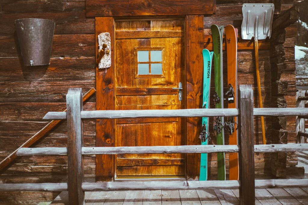 three sets of faction skis lean up against wooden cabin door