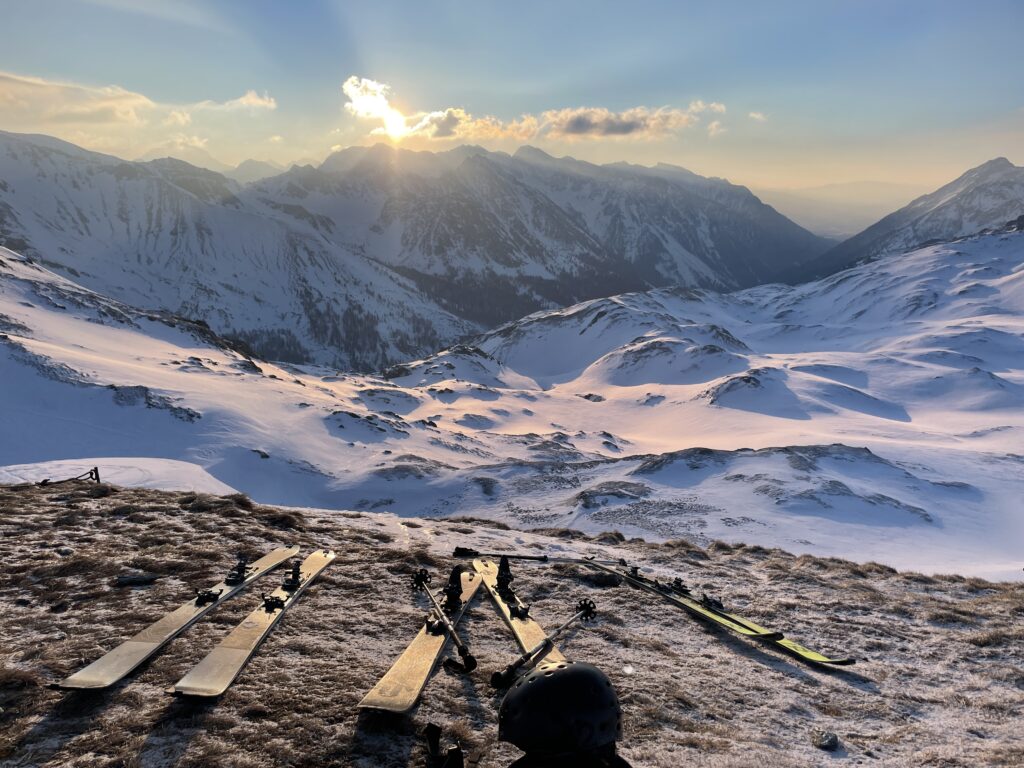 early morning ski tour scenes at top of mountain as sun rises. snow is shining from sun's reflection as skis lie on the ground