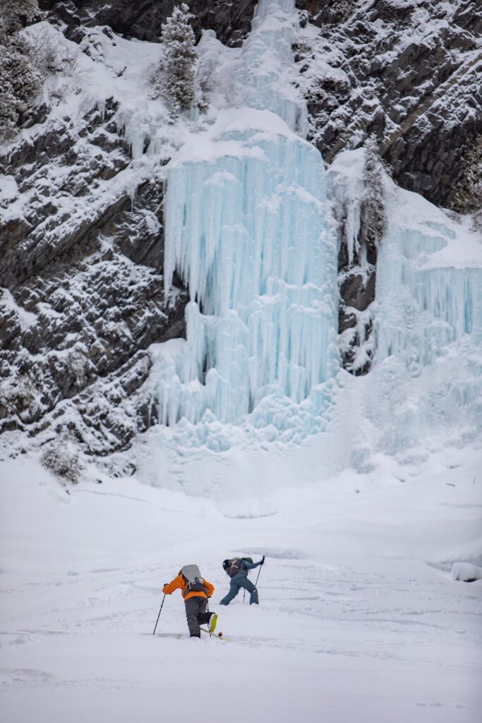 two mountaineers climb towards rock cliff and frozen waterfall