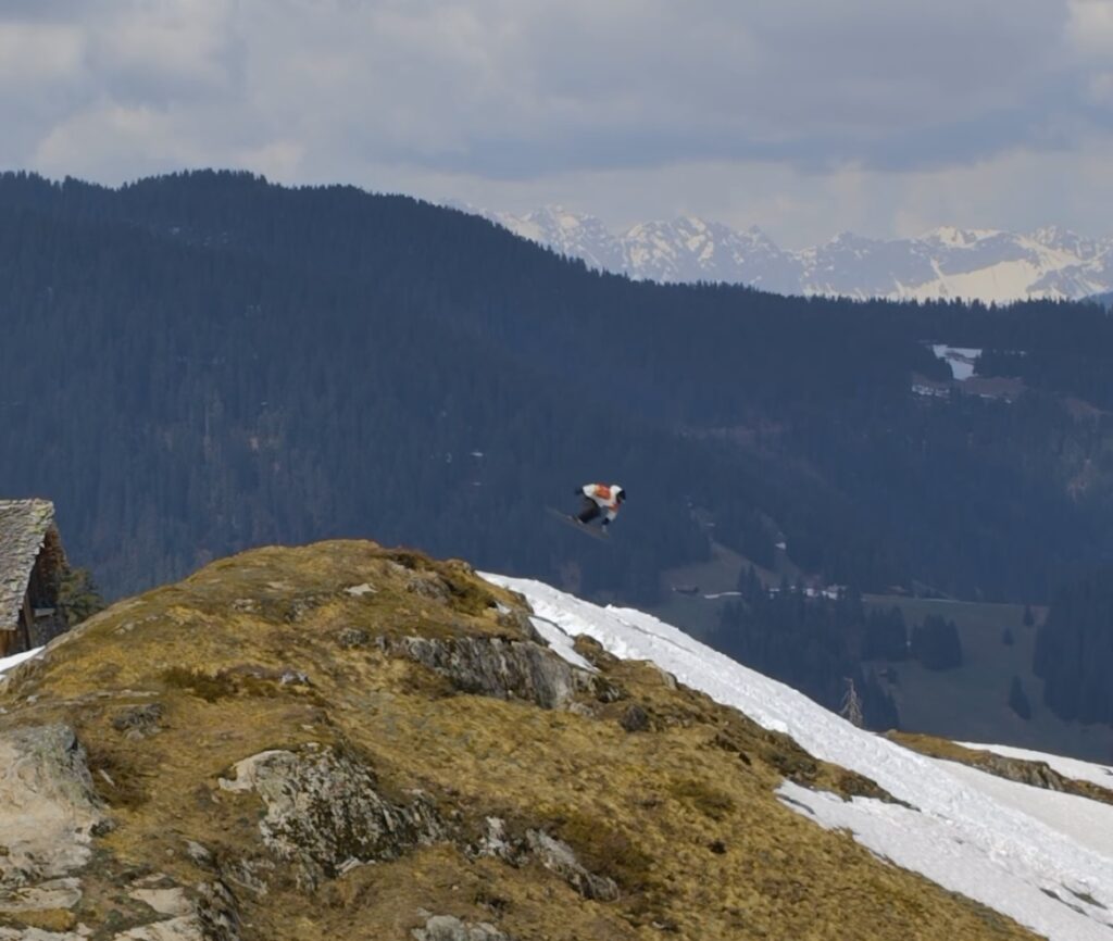 skier candide thovex jumps over grassy hill in nearly snow-less landscape