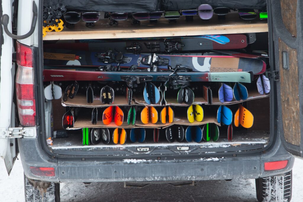 skis are stacked in layers in the boot of a van. All have colourful bases