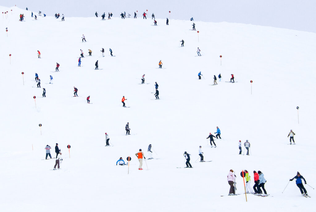 a ski piste full of skiers like ants dotted all over the hill