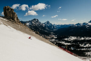 open carve on piste with rocks, sun and brown ground to the side of the piste on show behind skier making arc turn