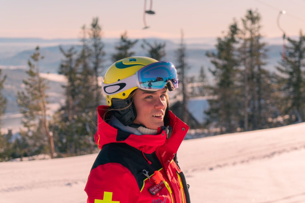 fmeale ski patroller in red looks into distance on a norwegian, warmly lit slope/piste