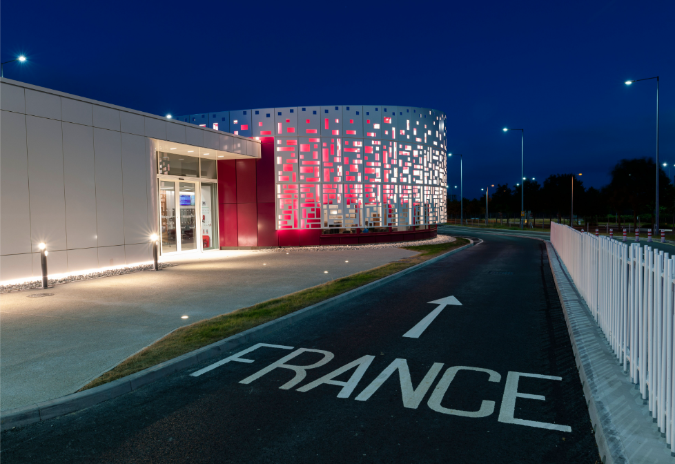 the road inside the Eurotunnel station pointing towards France next to the Flexiplus club building. It's night time and lights are shining bright