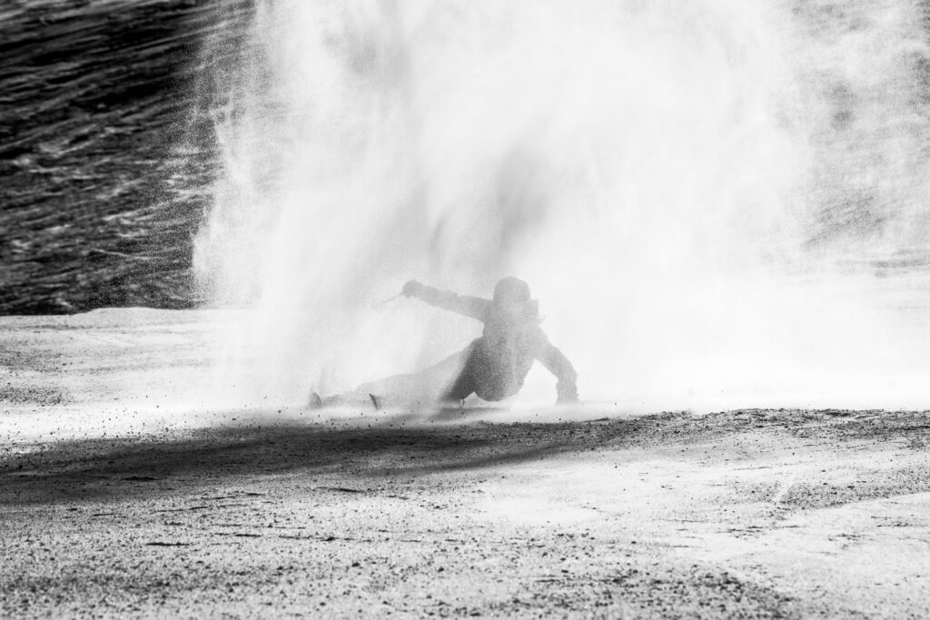 a skier with arms out carves through a light dust cloud, the photo is shot in black and white