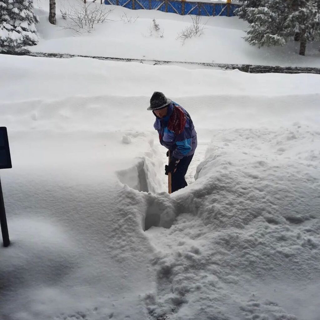 man in trad Italian mountain dress digs out feet of fresh snow from what's probably his doorway/front path