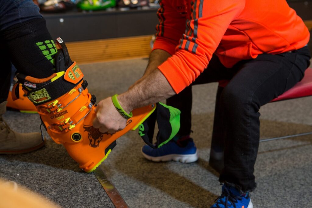 headless man (from image cut off) in orange fits a customer with an orange ski boot in a shop