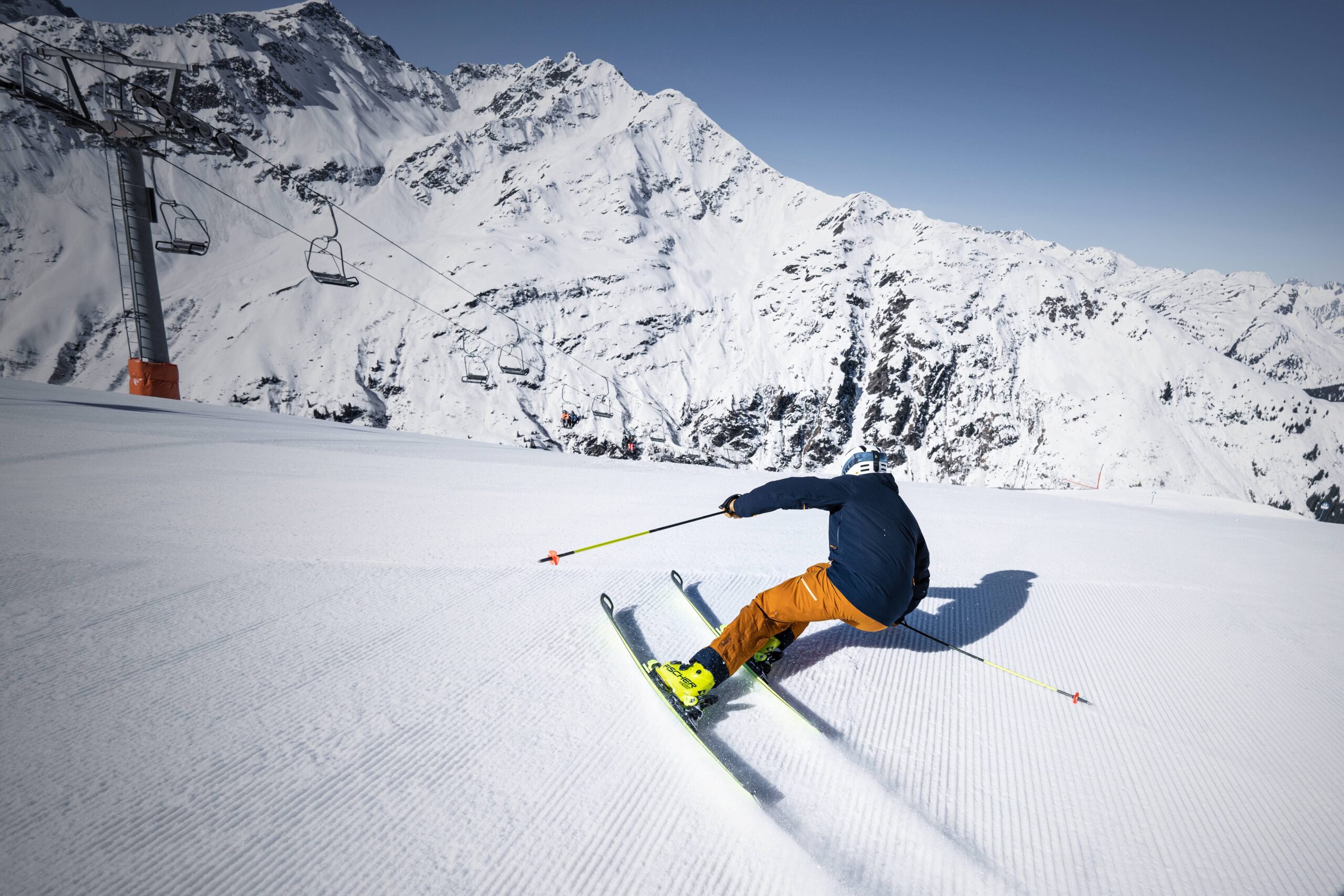 a perfect carve turn by a skier on groomed piste taken from behind with a old looking chair lift seen in the side of the shot