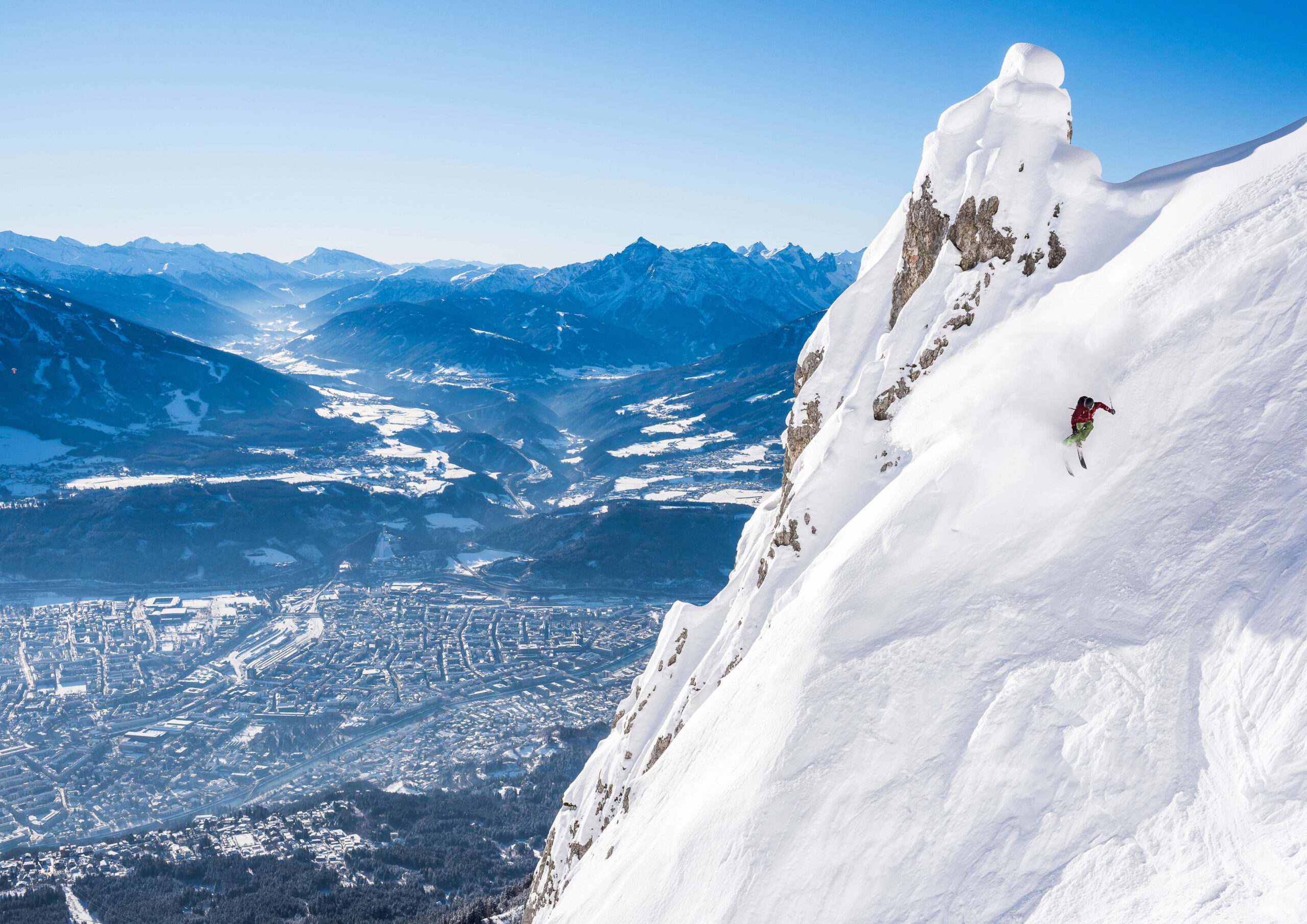 skier is on a very steep face making a turn, with the valley city of Innsbruck below.