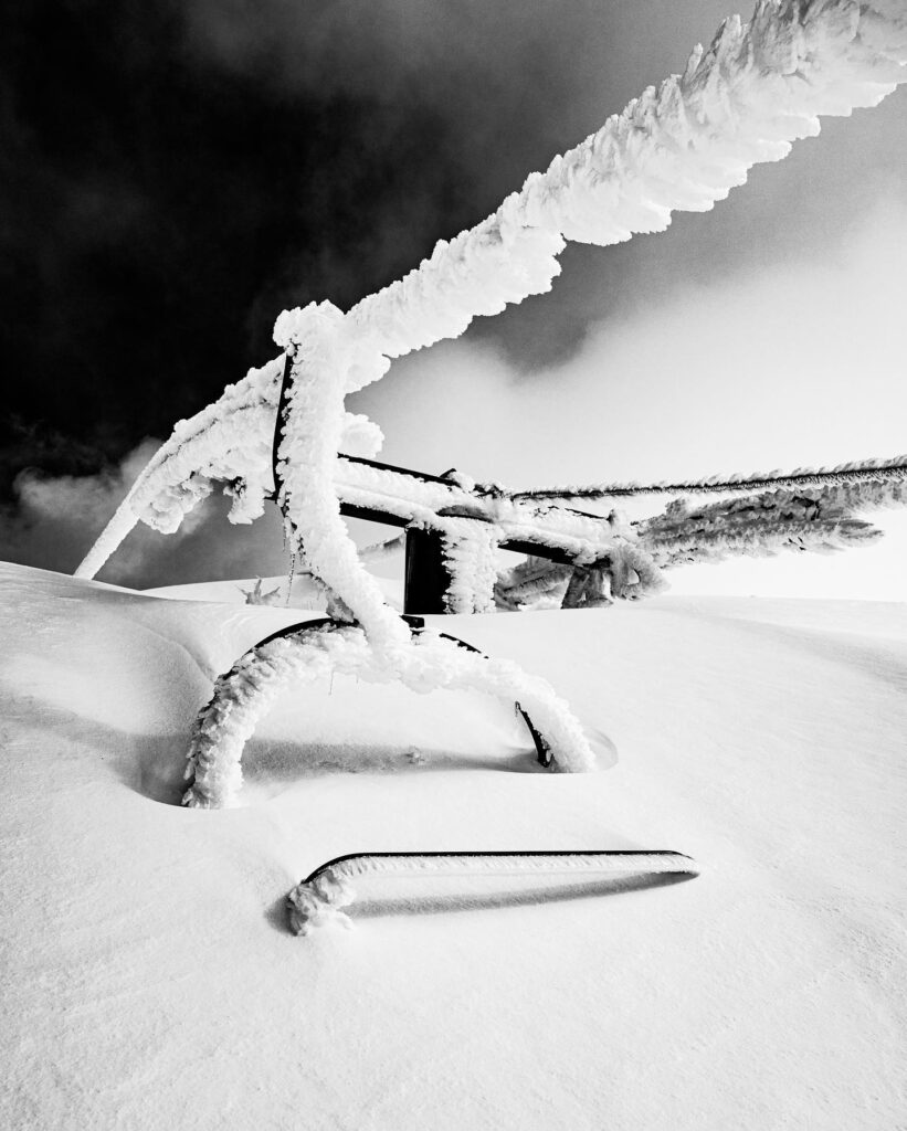 black and white image of a chairlift almost buried in snow. Rime on cable