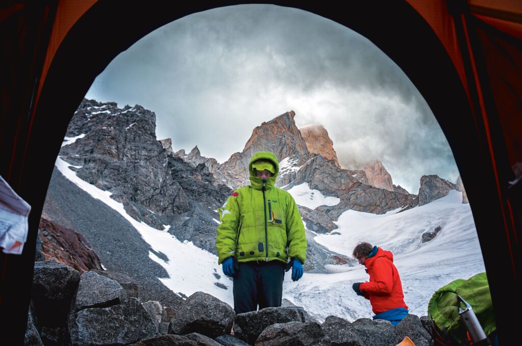 photo taken from inside a tent to outside of mountaineers framed against the summit