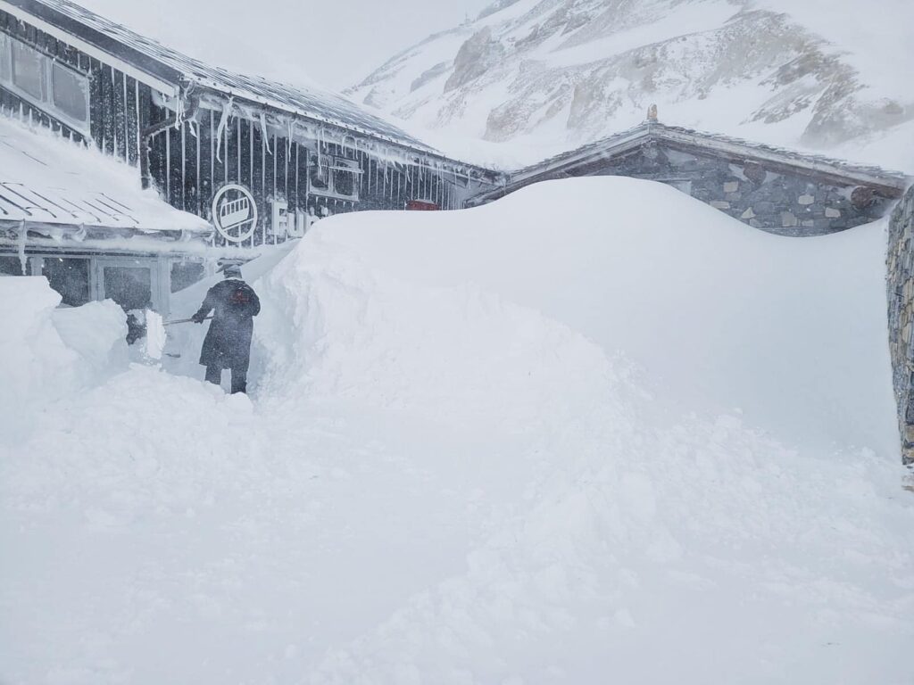a person digs out a chairlift station under very heavy snow