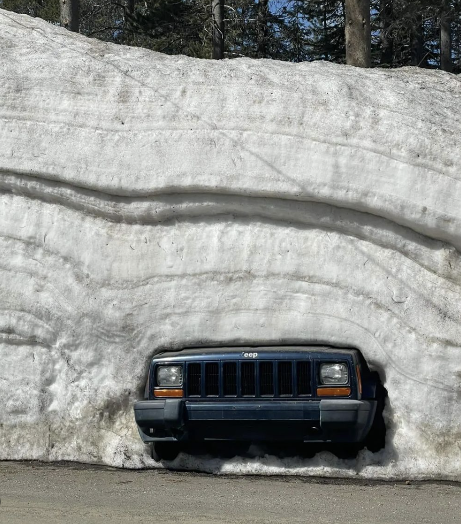 a jeeps front bumper is visible, buried deep in metres of snow, as the snow melts, the car becomes visible again