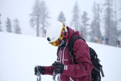 a skier in a white helmet looks down towards their feet in a very snowy setting, trees blurred behind