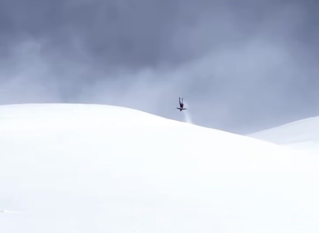 skier half way though backflip off a natural roller/kicker in fresh snow