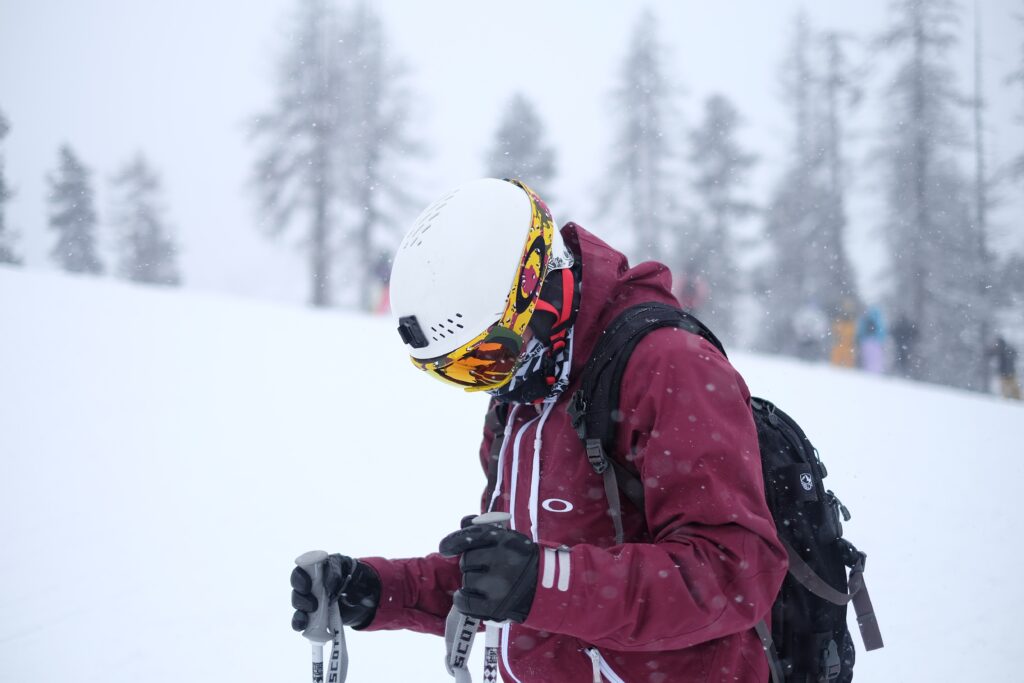 skier in white helmet and maroon jacket stands still looking at the floor