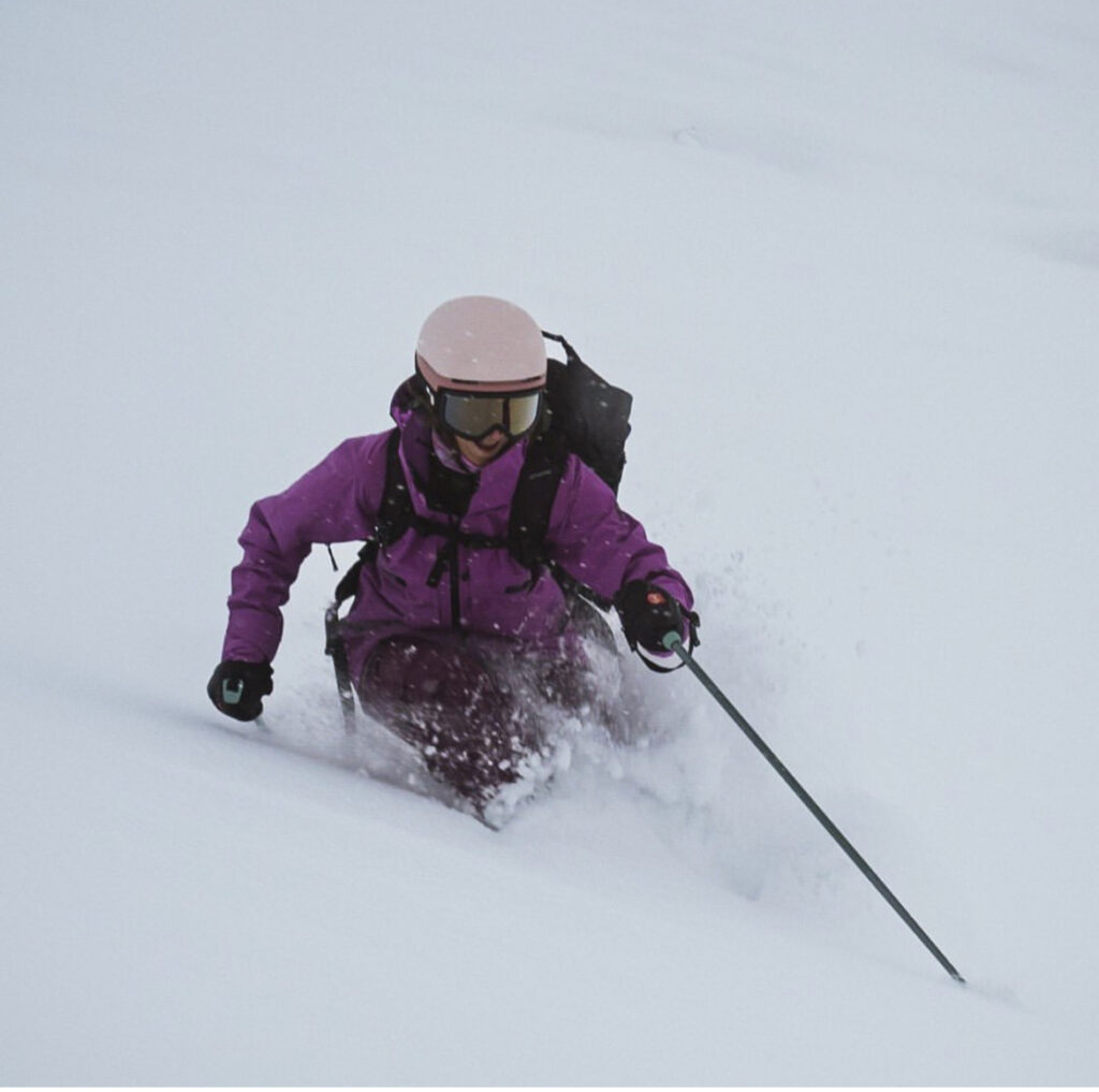 skier in purple jacket and pink helmet skis fresh snow. Nothing else in shot except skier on turn