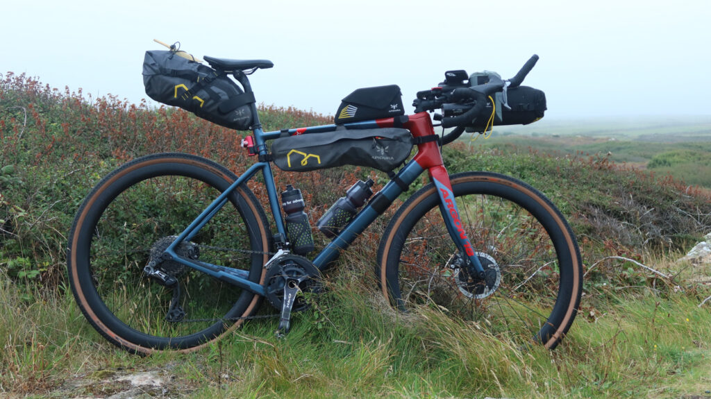 A bikepacking setup - bike propped up, ready to go, outside in wet-looking countryside