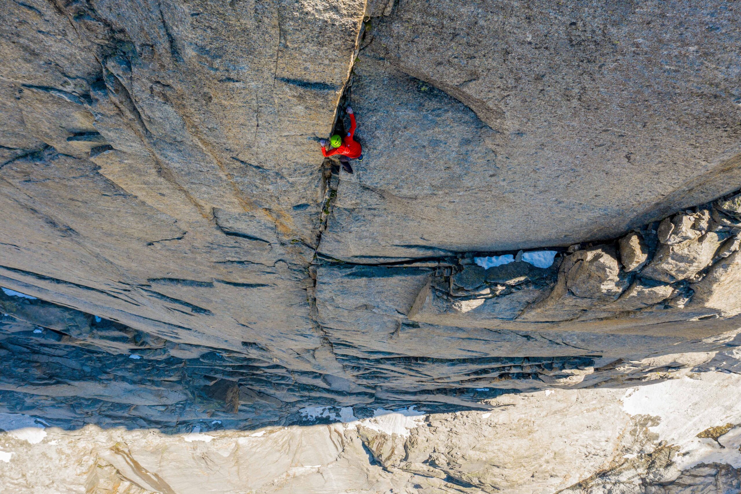 a sheer rock face, hundreds of metres tall, is shot from above as a small climber, free climbs the rock face