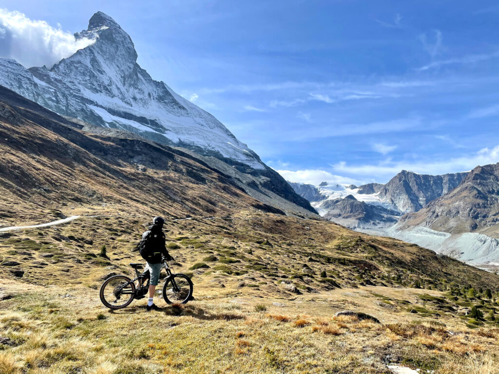 The matterhorn, dusted in snow and greener pastures surround it with a biker stopped to take a look over the iconic mountain
