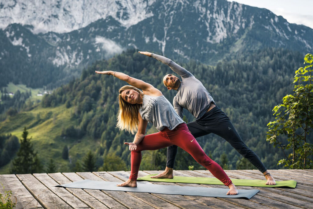 a man and women stretch it out sideways on a platform in the green mountains