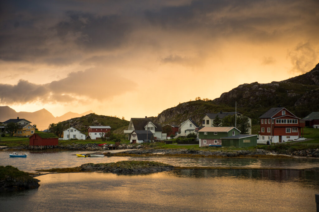 A fjord town at low light, red houses and rocky hills in shadow, with light bouncing off the water