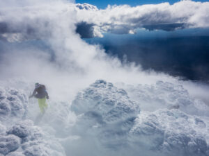 skier in mist walks through clouds amid piles of snow in lumpy mushrooms climbs uphill