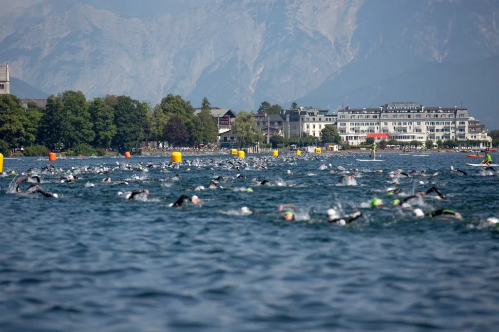 heads, arms and splashes of dozens, if not hundreds of swimmers, in a lake surrounded by mountains