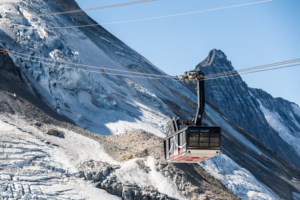A cable car is mid-way through a journey, icy-rocky slopes of a glacier behind it