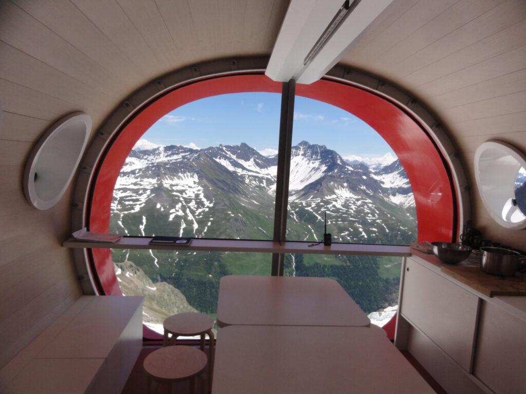 inside a space-age capsule, with views through the window-wall over snow streaked mountains outside