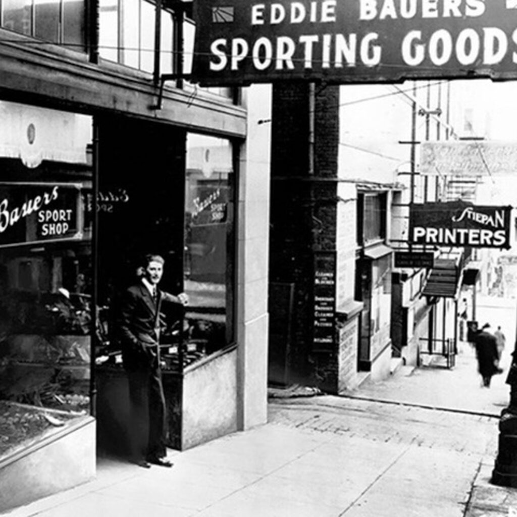 black and white photograph of a shop front, Eddie Bauer Sporting Goods, a man in a suit leaving the glass-fronted shop