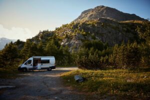 A camper sits in the shadow of a summery scene in the mountains, with the rocks catching the sunlight and yellow wildflowers picking out colour