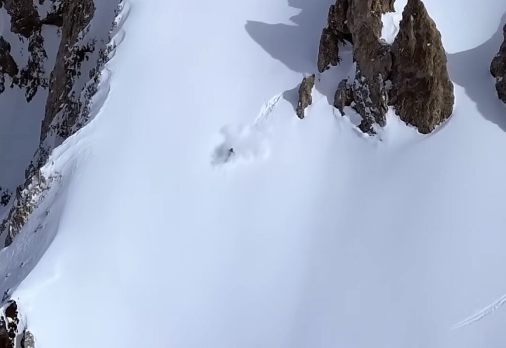 one skier, shot from drone, on a beautiful line down an untouched face below cliffy rocks