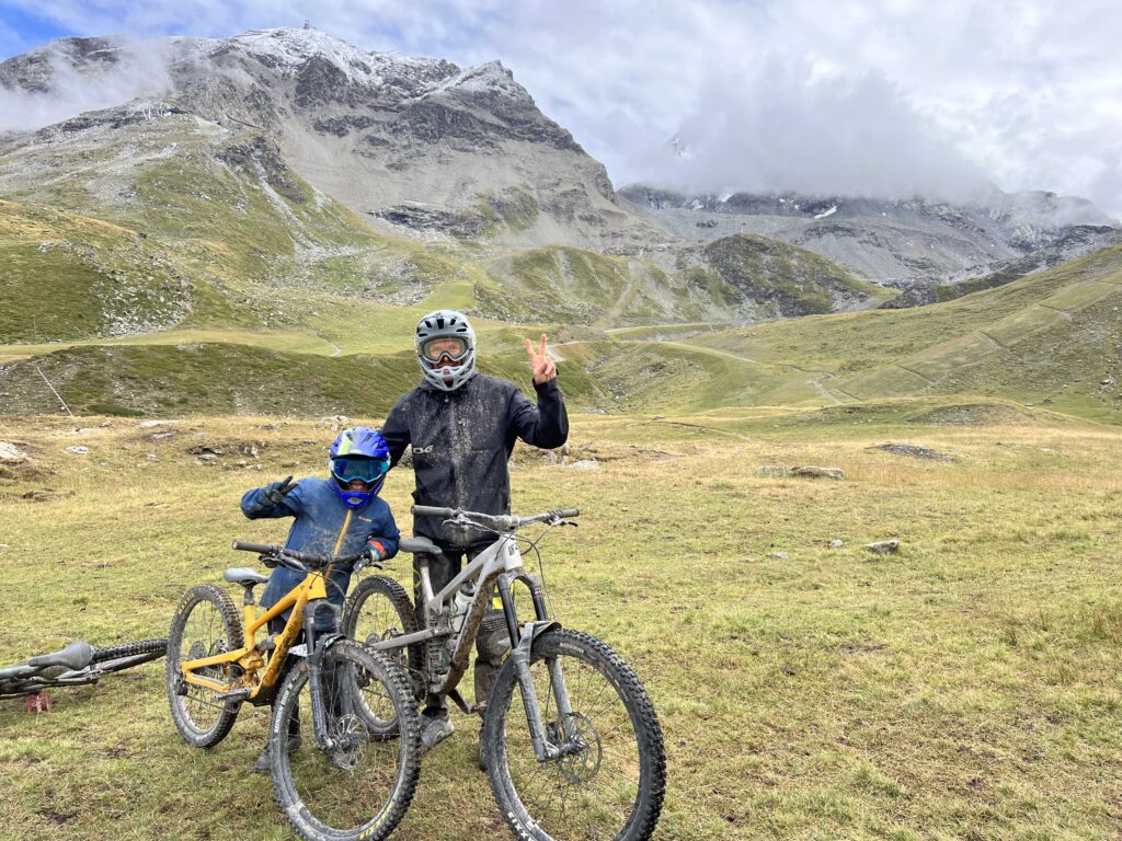 father and son, head to toe in mountain biking gear pose for photo in the mountains, dirty from biking, making peace fingers