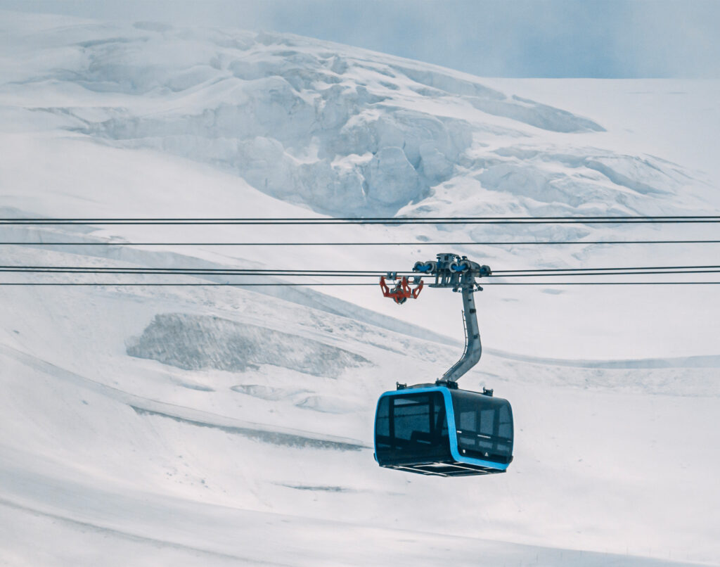 A new blue cable car is mid-journey over snow and under a glacier