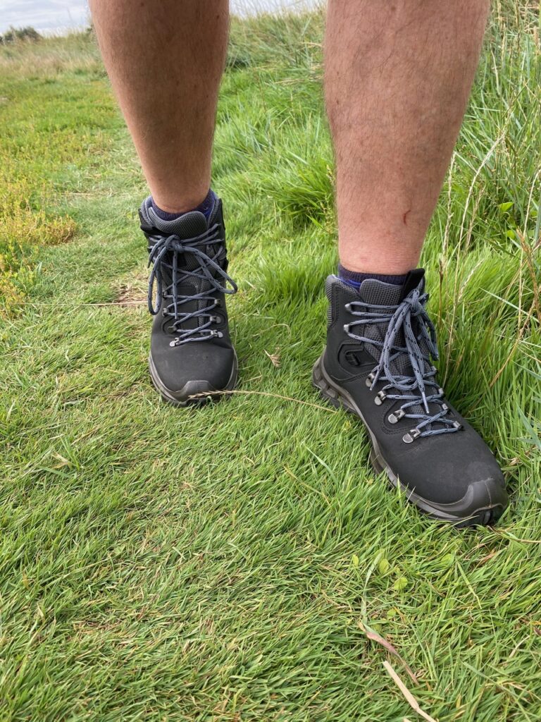 A men's hiking boot (vegan it turns out) is shot in action on green grass, with bare legs