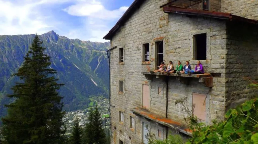 five women sit on a ledge of an abandoned ski station, in the mountains in summer
