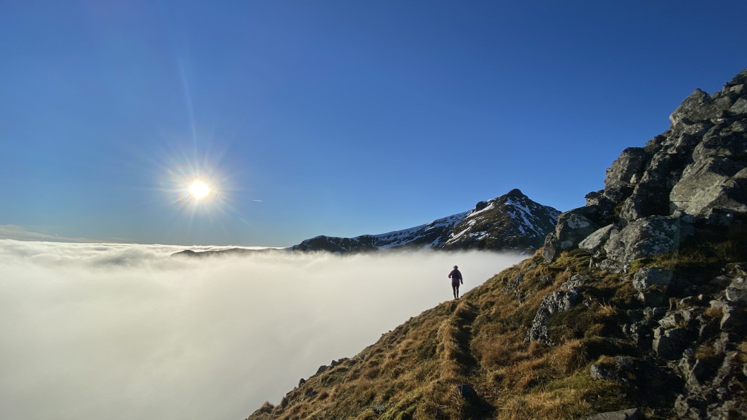 a solo runner above the clouds on a rocky mountain trail, sun shining