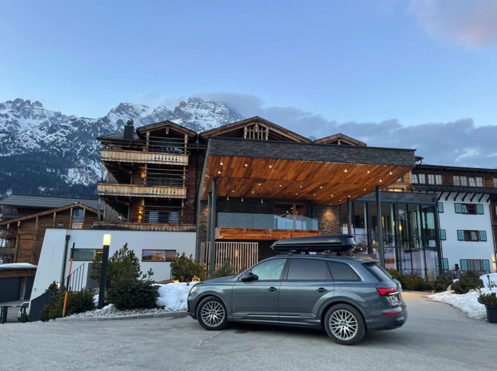 A car parked outside the fancy entrance of a wooden eco hotel in the mountains