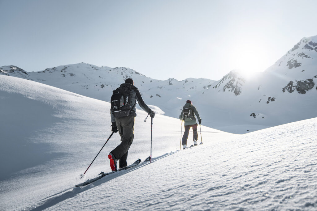 two ski tourers in a snowy landscape skin away from camera towards a low sun