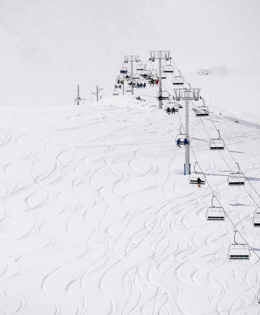 a chairlift is shot, with people sat on it, and ski lines beneath