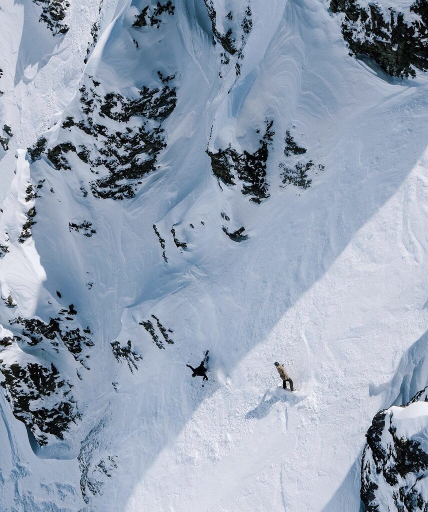 snowboarder and skier on steep off piste descent, surrounded by rocks (picture taken by a drone)