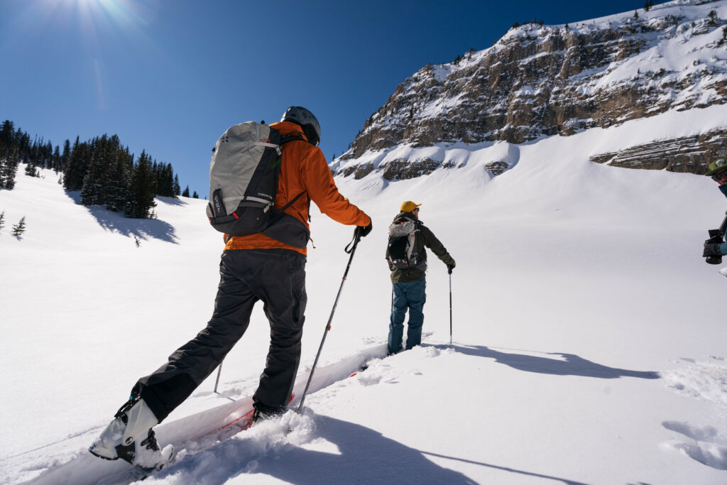 two ski tourers skin up a mellow slope near the top of a mountain