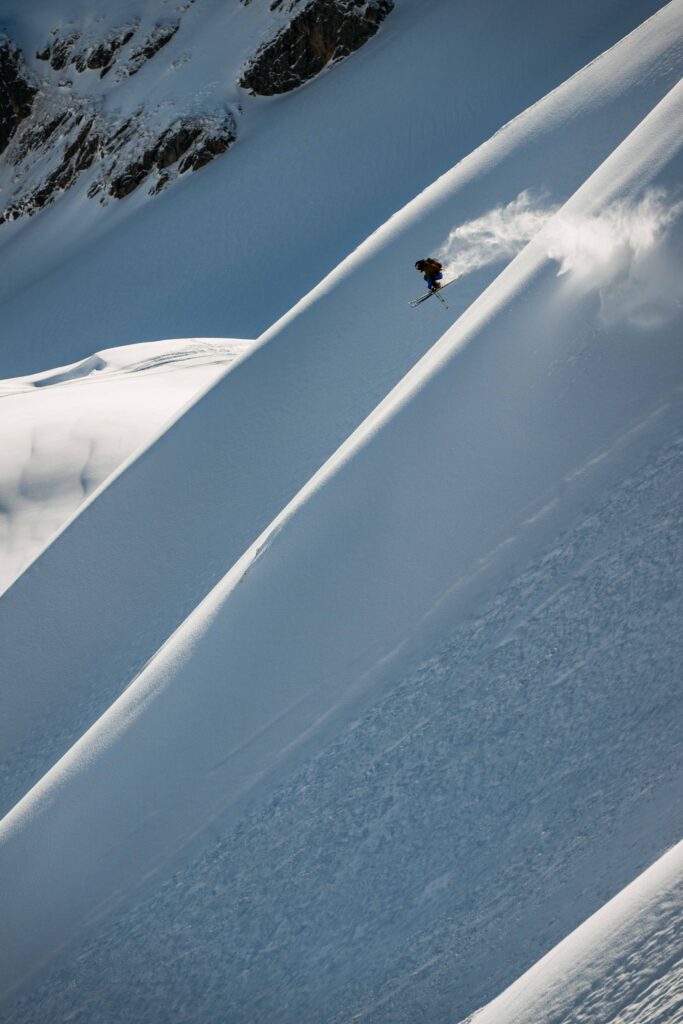 A skier takes air on an untouched face, the spines of snowy mountain picked up by sunlight.